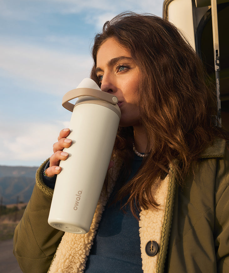 A person drinking from a light-colored insulated bottle